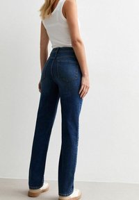 Högmidjade raka jeans i mörkblå denim. Har bakfickor och minimala sömnadsdetaljer. Kombineras med en vit linne.