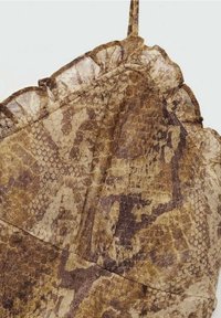 Gros plan sur un tissu imprimé serpent marron et beige avec un bord froncé le long du bord supérieur, montrant les détails de la texture et du motif.