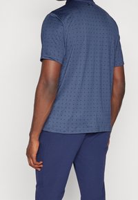 Polo bleu marine à manches courtes avec un motif texturé de petits points, tissu lisse et col classique, associé à un pantalon assorti.