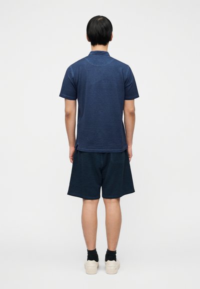Μπλε ναυτικό πόλο μπλουζάκι και αντίστοιχο σορτς. Το μπλουζάκι έχει κλασικό γιακά και κοντά μανίκια, ενώ το σορτς είναι σε άνετη εφαρμογή και έχει μήκος μέχρι το γόνατο.
