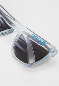 Selge atsetaatpäikeseprillid tumedate läätsedega. Roheline Oakley logo peadükil. Sile tekstuur, ümar kuju.