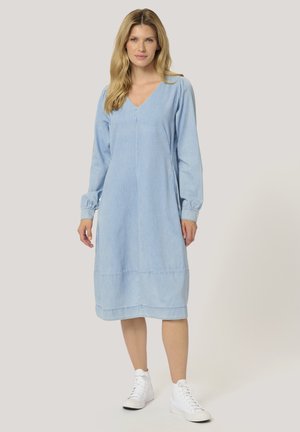 Hellblaues Denim-Kleid mit V-Ausschnitt, langen Puffärmeln und gerafftem Saum. Kombiniert mit weißen Sneakers für einen lässigen Look.
