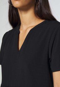 Black short-sleeve top with a subtle V-neckline, made from smooth fabric featuring a relaxed fit and no visible patterns or embellishments.
