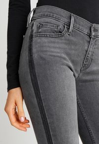 Jeans de mezclilla gris con un diseño ajustado, detalles en los laterales y bolsillos estándar. La tela tiene una textura suave y ligeramente deslavada.