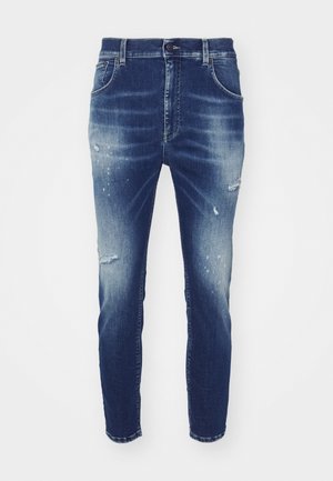 Jeans iz džinsa v srednjo modrem pranju s pobledelimi območji, uničenimi podrobnostmi in zoženim krojem. Ima klasično zasnovo s petimi žepi in zankami za pas.