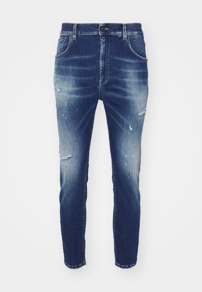 Džinsi no denima vidējā zilā mazgājumā ar izbalējušām vietām, nodilušiem elementiem un sašaurinātu piegriezumu. Tam ir klasiskā piecu kabatu dizains un jostas cilpas.