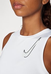 Hvit, ermeløs, atletisk T-skjorte med rund hals. Har en svart Nike-logo på venstre brystområde. Glatt tekstur.