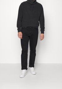 Sudadera negra con cuello alto y cordón, combinada con jeans negros y zapatillas blancas. Tejido suave, ajuste relajado.