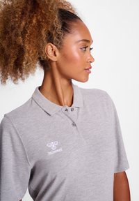 Szara koszulka polo wykonana z miękkiego materiału, z kołnierzykiem i trzema guzikami. Logo Hummel jest haftowane na białym tle po lewej stronie klatki piersiowej.