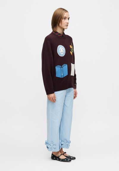 Burgunderfarget strikkegenser med broderte lapper, lyseblå vide bukser med blomsterdetaljer, og svarte flate sko med pynt.