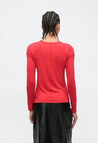 Pikad varrukad punane topp, mis on istuva lõikega, ümara kaelusega ja lihtsa õmblusega. Sobitatuna musta läikiva nahast seelikuga.