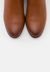 Bottes à la cheville en cuir marron avec une texture lisse et des bouts arrondis, présentant une légère brillance et une semelle noire.
