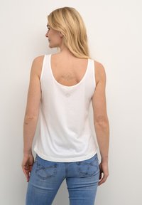Weißes Baumwoll-Top mit Rundhalsausschnitt und Racerback-Design, mit abgerundetem Saum. Tragen Sie es mit hellblauen Jeans mit minimalen Used-Effekten.
