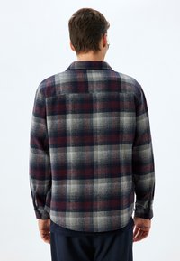 Geruite flanellen shirt met marineblauwe, grijze en rode kleuren. Zachte textuur, afgeronde zoom en knoopsluitingen op de mouwen.