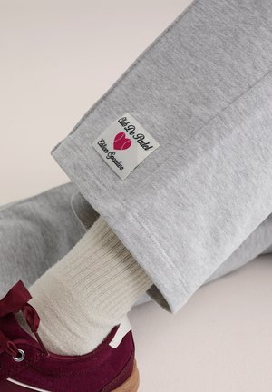 Sivé teplákové nohavice majú štítok s logom "Club De Padel" s ružovými akcentmi. Celý vzhľad dopĺňa krémová rebrovaná ponožka a gaštanová obuv.