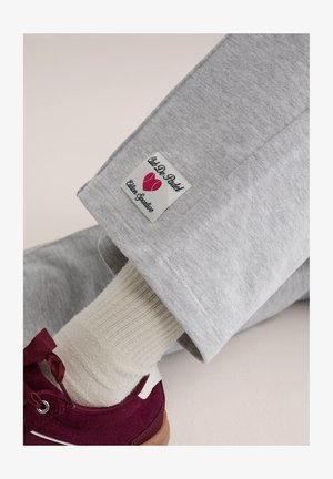 Szare dresy z metką z logo "Club De Padel" z różowymi akcentami. Dopełnieniem są kremowa, prążkowana skarpetka i bordowy but.