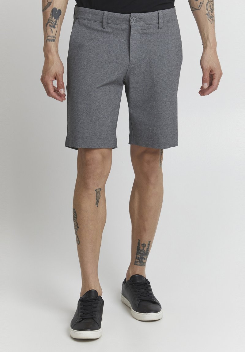Shorts gris en matériau texturé, avec une coupe droite et deux poches latérales. Associés à des baskets noires pour un look décontracté.