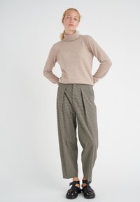 Beige turtleneck sweater paired with patterned, high-waisted, pleated gray trousers. Black sandals with adjustable straps complete the outfit.