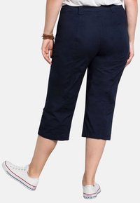Pantaloni cropped navy realizzati in tessuto resistente con una texture liscia, dotati di dettagli sulle cuciture laterali e di un taglio dritto, abbinati a sneakers bianche.