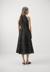 Mustat pitsiset olkaimeton mekko, jossa on istuva yläosa, levenevä hame ja monimutkaiset kukkakuviot. Yhdistetty mustiin korkokenkiin.