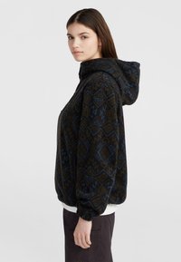 Veste en polaire à capuche de couleur marron foncé avec un motif géométrique bleu et kaki. Elle présente une texture douce, des poignets élastiques et une poche frontale.