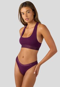Fioletowy sportowy biustonosz i dopasowany string o gładkiej fakturze. Biustonosz posiada szerokie ramiączka oraz wytłoczone logo na pasku.