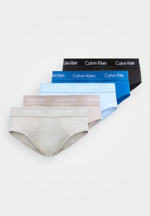 Fem par Calvin Klein herrestrømper i sort, blå, lyseblå, beige og grå, stablet diagonalt på en hvid baggrund.