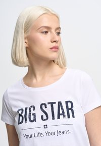 Bílý tričko s kulatým výstřihem a krátkými rukávy. Design na přední straně: "BIG STAR" v opotřebované námořnické modři, s heslem pod ním.