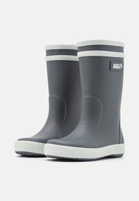 Bottes en caoutchouc grises avec des accents blancs, présentant une texture lisse, un bout arrondi et un profil de semelle prononcé. Logo de la marque visible.