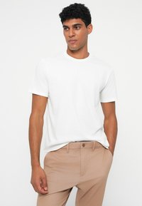 Hvit T-skjorte med korte ermer og rund hals, laget av glatt stoff, sammen med lyse beige bukser med klassisk knappefeste.