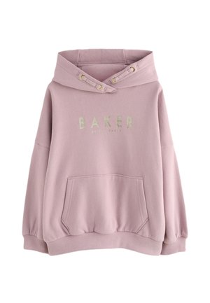 Kvinde iført oversized støvet lyserød hættetrøje med hvid sløjfe og teksten "Paris Baker" på ryggen, kombineret med sorte bukser.