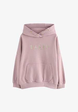 Kobieta nosząca oversize różową bluzę z kapturem z białą kokardą i napisem "Paris Baker" na plecach, w połączeniu z czarnymi spodniami.