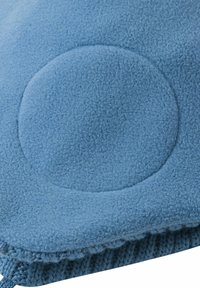 Niebieska tkanina polarowa z okrągłym uwypuklonym wzorem, z dzianinowym dolnym brzegiem. Materiał wydaje się miękki i gruby.