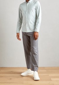 Jasnozielona koszula na guziki, szare dopasowane spodnie oraz białe trampki. Gładki materiał o klasycznym wyglądzie; prosty krój i casualowy design.