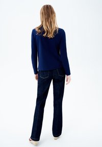 Navy blauwe longsleeve top gecombineerd met donkerblauwe flared jeans. De top heeft een gladde textuur, terwijl de jeans contrasterende stiksels en een lichte stretch hebben.