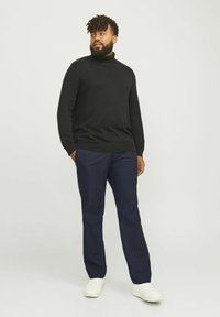Schwarzer Strick-Turtleneck-Pullover, marineblaue Hose und weiße Sneakers. Das Outfit zeichnet sich durch eine lockere Passform, weichen Stoff und ein einfaches Design aus.