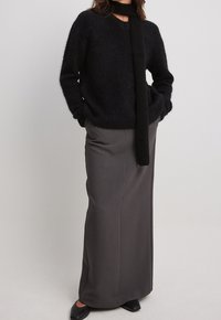 Pull noir duveteux avec un col en V et une écharpe attachée, associé à une longue jupe grise. Des chaussures noires complètent la tenue. Design simple et élégant.