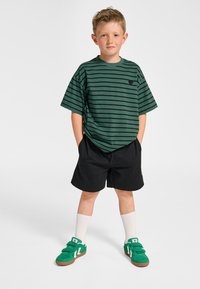 Grönrandig t-shirt, korta svarta shorts, vita strumpor och gröna sneakers med bruna sulor. Har en liten logotyp på tröjan.