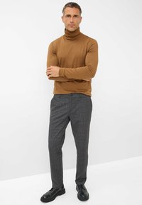 Maglione a collo alto marrone e pantaloni a quadri grigi. I pantaloni presentano un motivo a scacchi e sono abbinati a scarpe nere.