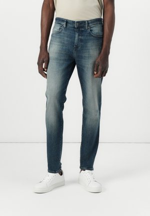 Mörkblå denimjeans med slim fit, med en blekt tvätt, femficksdesign och ljusa sömmar. Kombineras med vita sneakers.