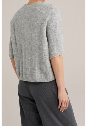 Person iført en lysegrå kortærmet strikket sweater og mørkegrå bukser med nålestriber, vist bagfra mod en ensfarvet baggrund.