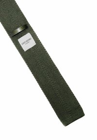 Grön vävd bälte med en texturerad yta, försedd med en silvrig metalldel och en rektangulär etikett med texten "JOHN HENRIC SWEDEN."