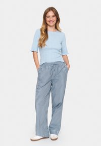 Lichtblauwe gebreide top met korte, uitlopende mouwen, gecombineerd met loszittende blauw-witte gestreepte broek, accentueerd met zakken.