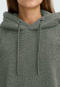 Grüne Fleece-Hoodie mit strukturierten Oberflächen, verstellbaren Kordeln und lockerer Passform.