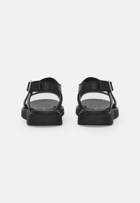 Black leather sandals featuring adjustable straps and a thick, textured sole. Open back design enhances breathability and comfort.