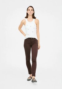 Balti baklanė su mažais papuošimais, derinama su tamsiai rudos spalvos aptemptais džinsais ir pilkais lygiais batais. Paprastas, kasdienis derinys.