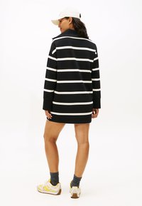 Melnā un baltā svītrainā kleita ar garām piedurknēm un apkakli. Modelis valkā baltu cepuri un sporta apavus ar dzelteniem akcentiem, demonstrējot ikdienišķu apģērbu.