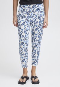 Witte broek met een blauw bloem- en paisleyprint, met een taps toelopende pasvorm en broekband. Gekozen in combinatie met zwarte slide sandalen.
