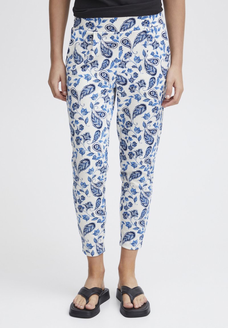 Witte broek met een blauw bloem- en paisleyprint, met een taps toelopende pasvorm en broekband. Gekozen in combinatie met zwarte slide sandalen.
