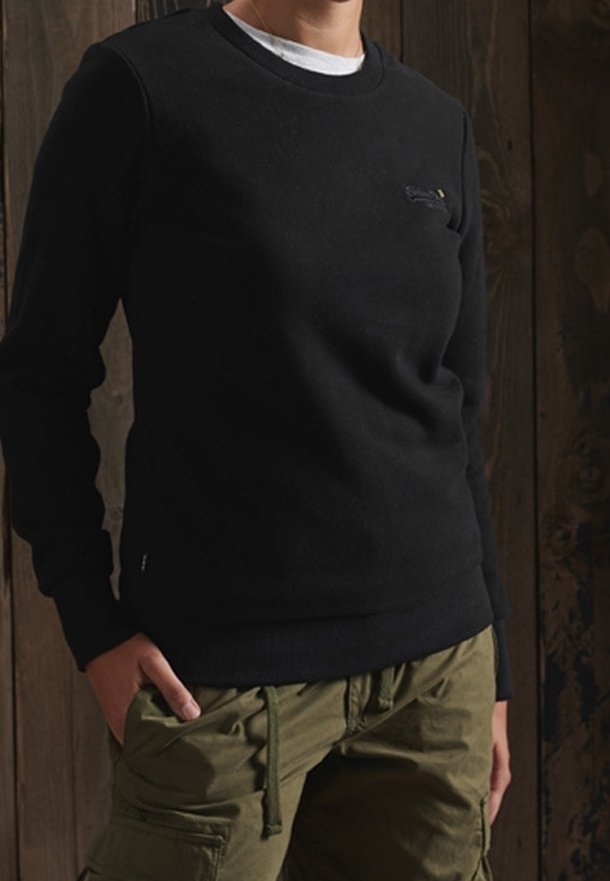 Sudadera negra con cuello redondo, hecha de una tela suave, que presenta un sutil logo en el pecho y puños y dobladillo de canalé texturizados.